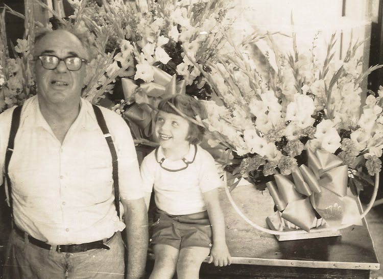 Spanning three generations of ownership, grandfather and granddaughter share a happy moment amidst the floral arrangements