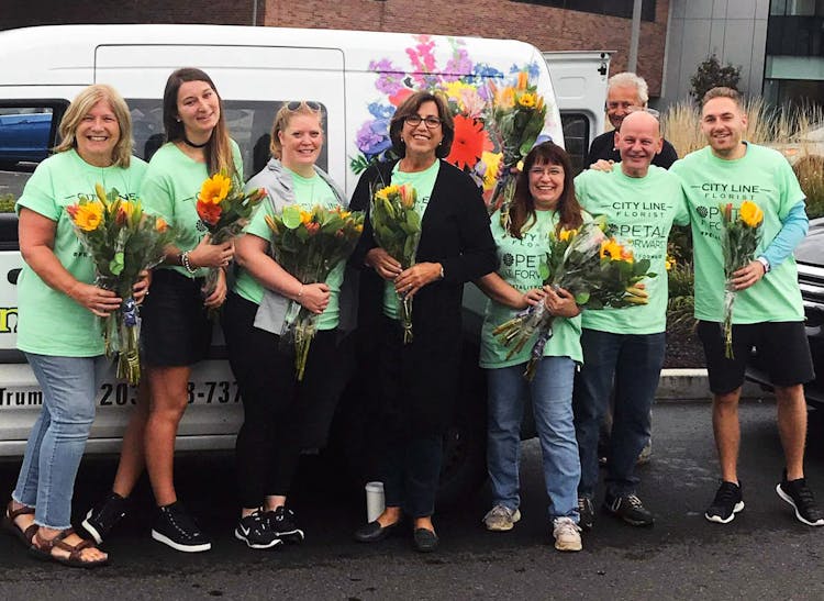 Our friendly team, gathered with bouquets, beside a branded delivery van